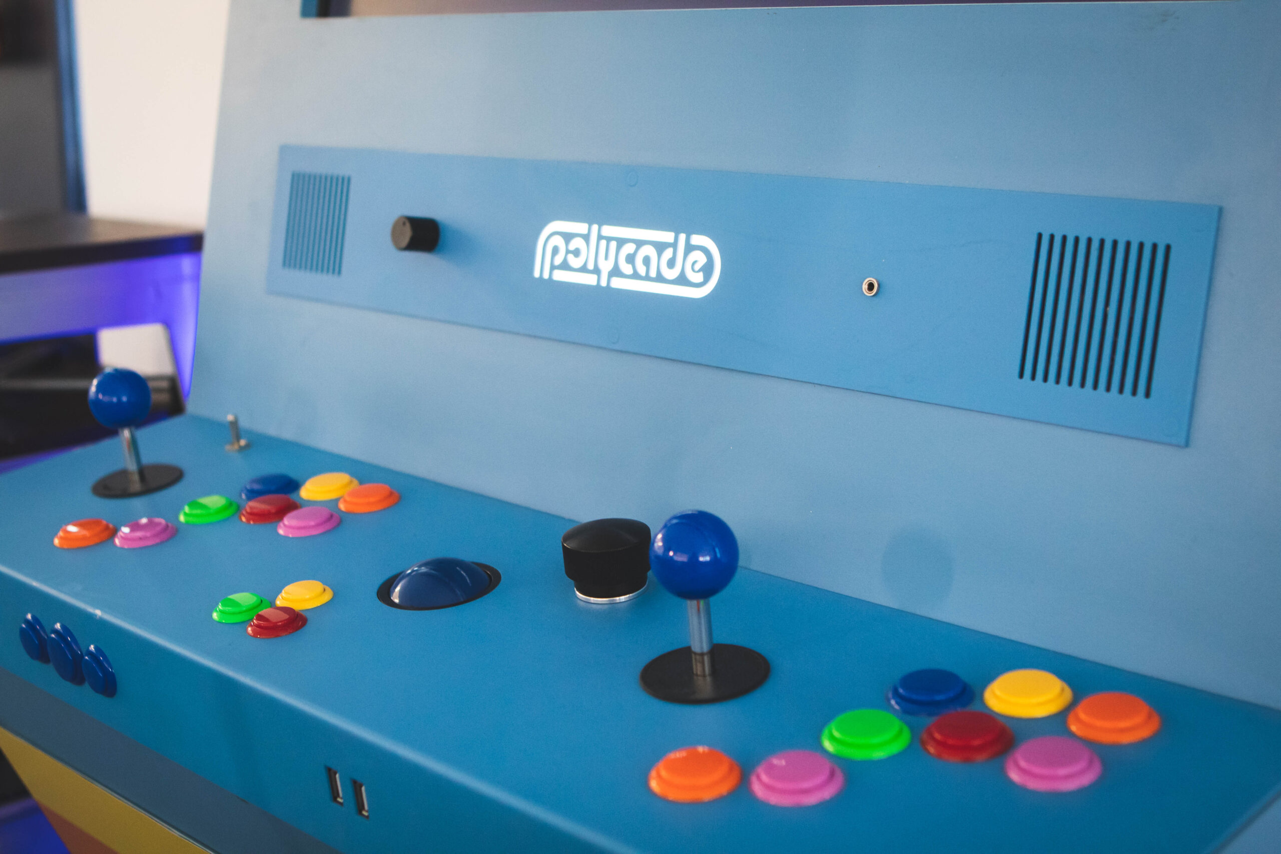 Closeup picture of blue Polycade arcade game with light blue dashboard, colorful buttons and black joysticks.