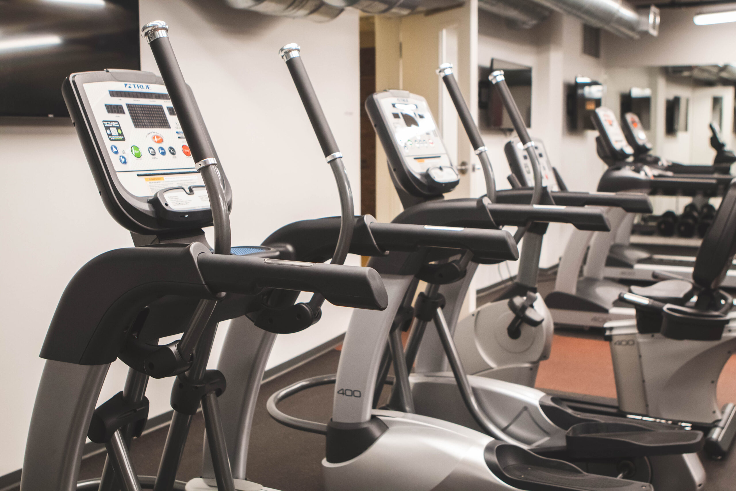 A row of cardio exercise equipment including elliptical machines and treadmills.