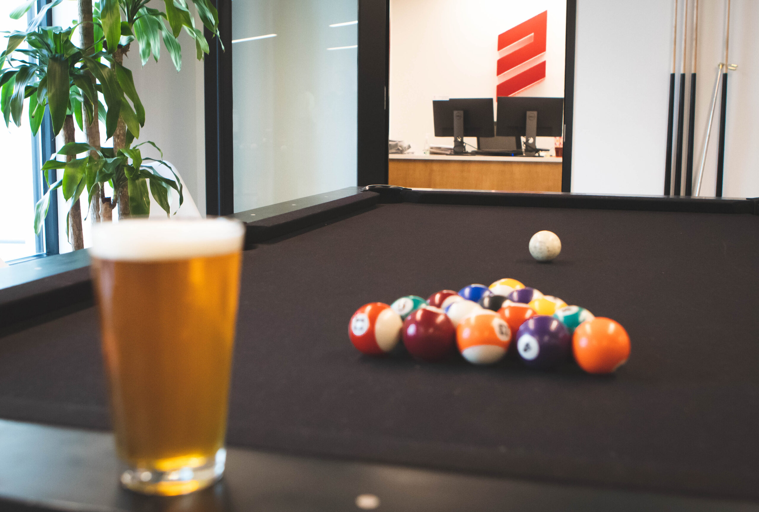 Photo of pint of beer and pool table with pint out of focus, beer glasses in focus, ELITE Transit Solutions E logo in the background.